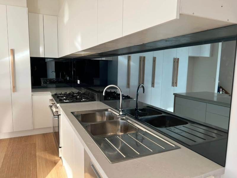 Modern white kitchen with black backsplash, island sink, and built-in cooktop, viewed from the counter