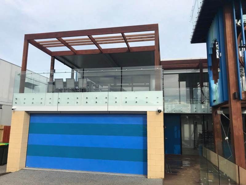 Modern two-story house with blue-striped garage door, glass balcony, and wooden roof pergola