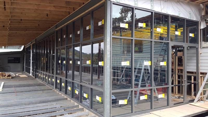 Glass storefront under construction with metal framing, exposed ceiling, and indoor scaffolding.