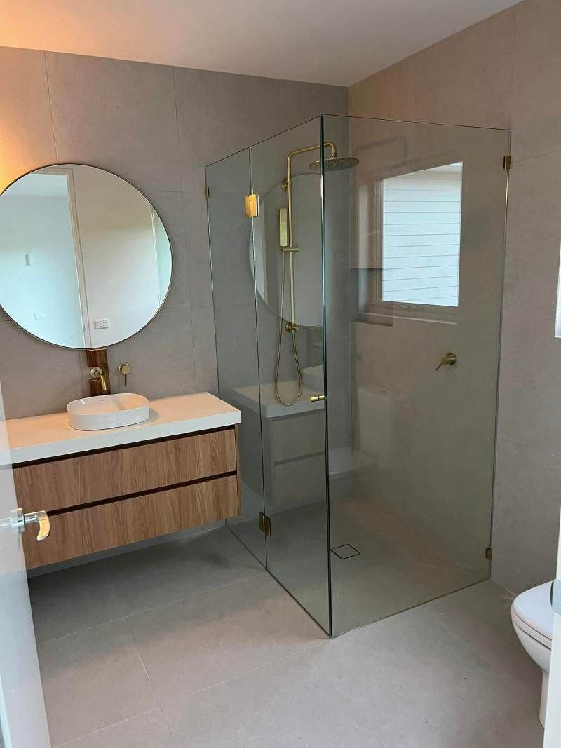 Modern bathroom with glass shower, round mirror, wood vanity, and white walls