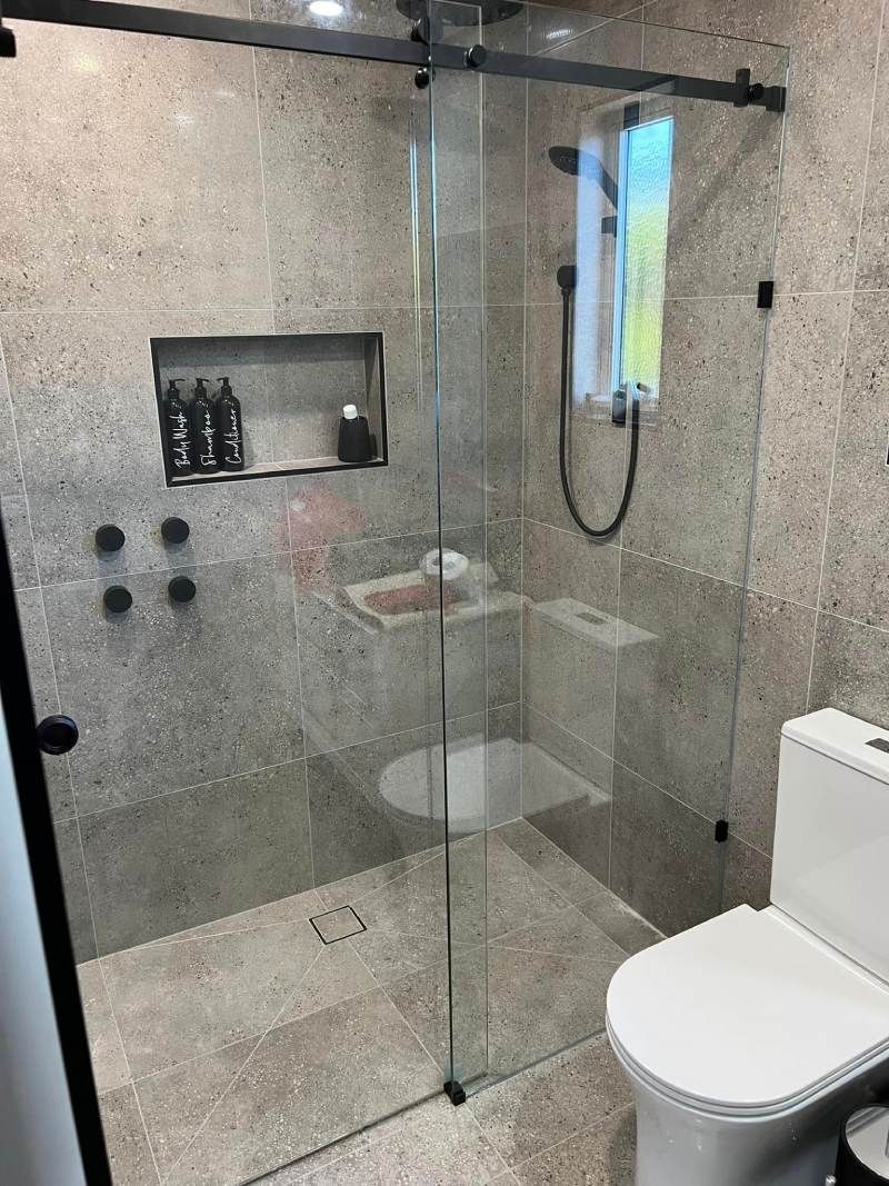 Modern glass shower with gray tile walls, built-in shelf, and white toilet in a bathroom