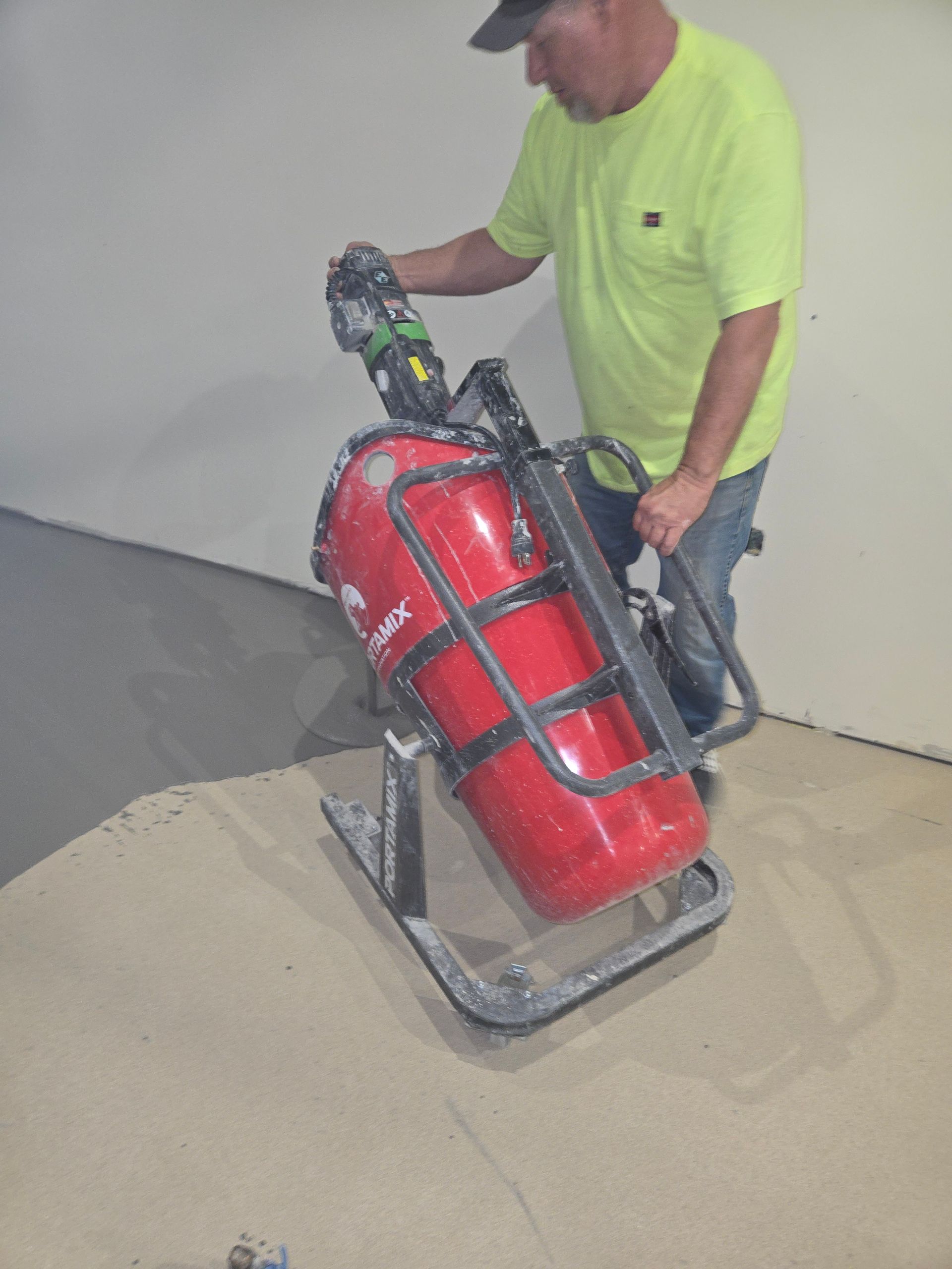 Person using a red concrete grinder on a concrete surface in a room.
