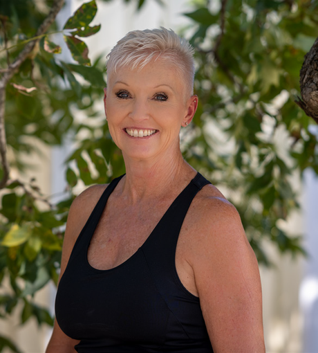 a woman in a black tank top is smiling in front of a tree .