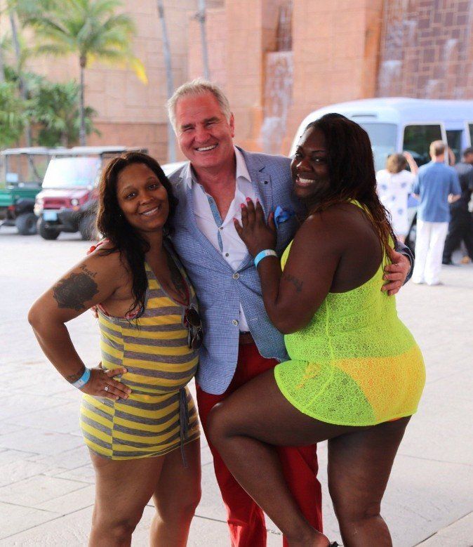 Man poses with two women in swimwear outside a resort.