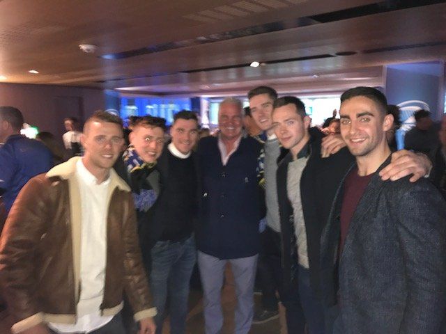 Group of men posing for a photo in a blue-lit interior. Some have arms around each other.