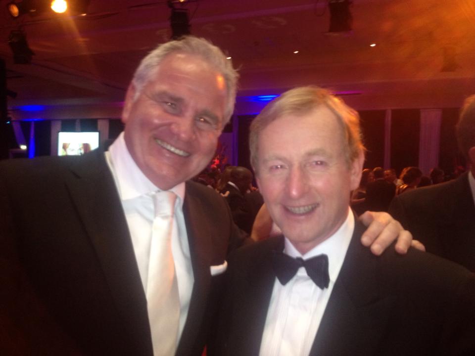 Two men in formal wear smile at the camera at an event.