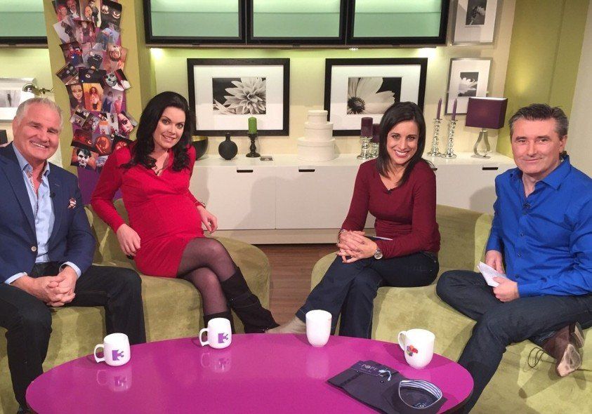 Four people seated on a couch in a studio, smiling. Two women and two men. Colorful backdrop, coffee mugs on table.