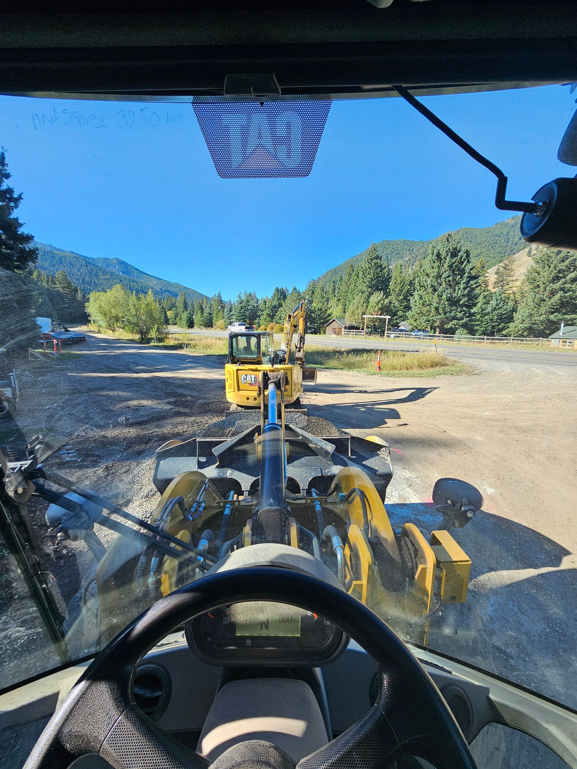 Two men are standing next to a bulldozer and an excavator in a field.