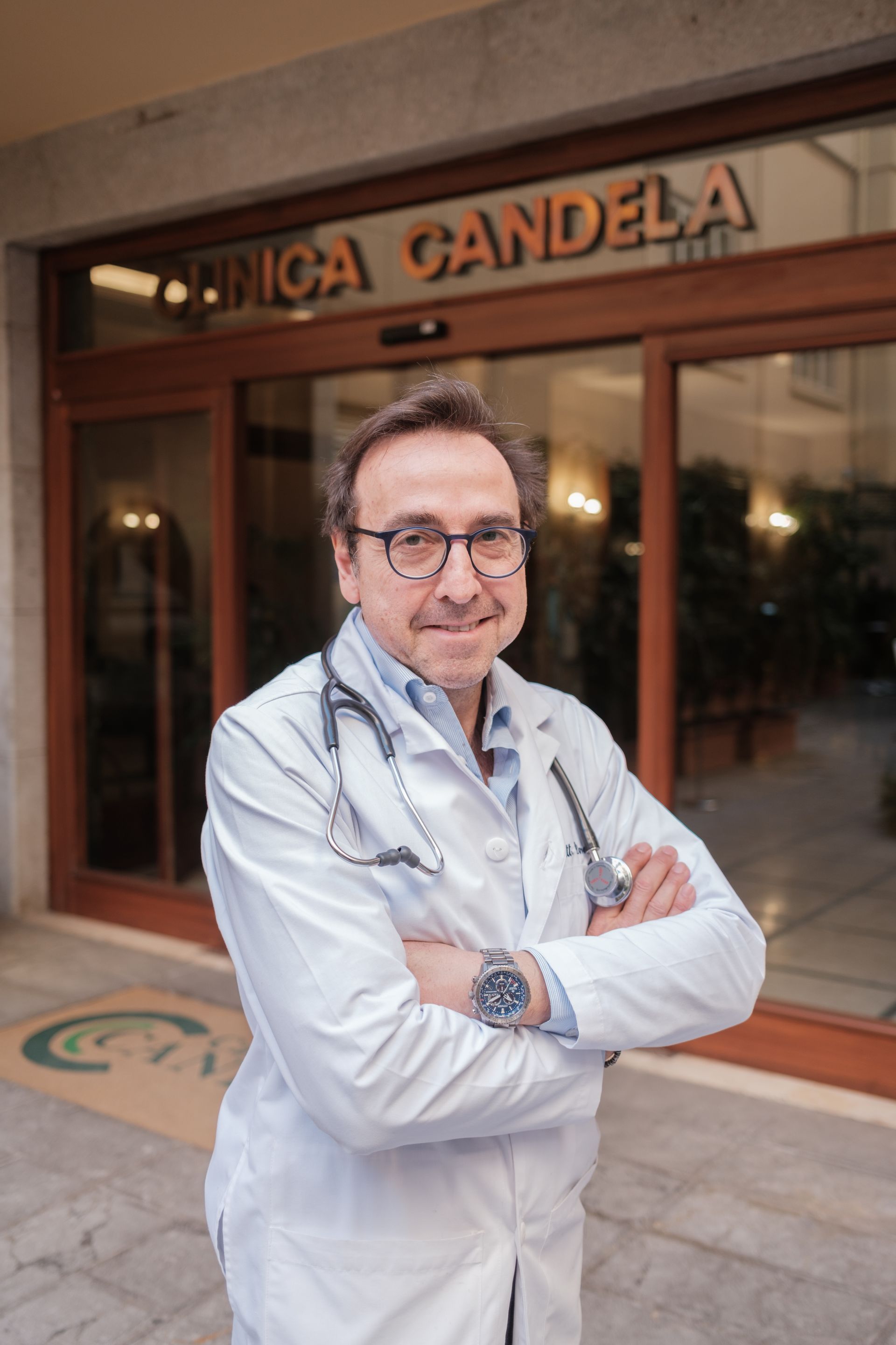 Un uomo in camice da laboratorio con uno stetoscopio al collo è in piedi davanti alla clinica candela