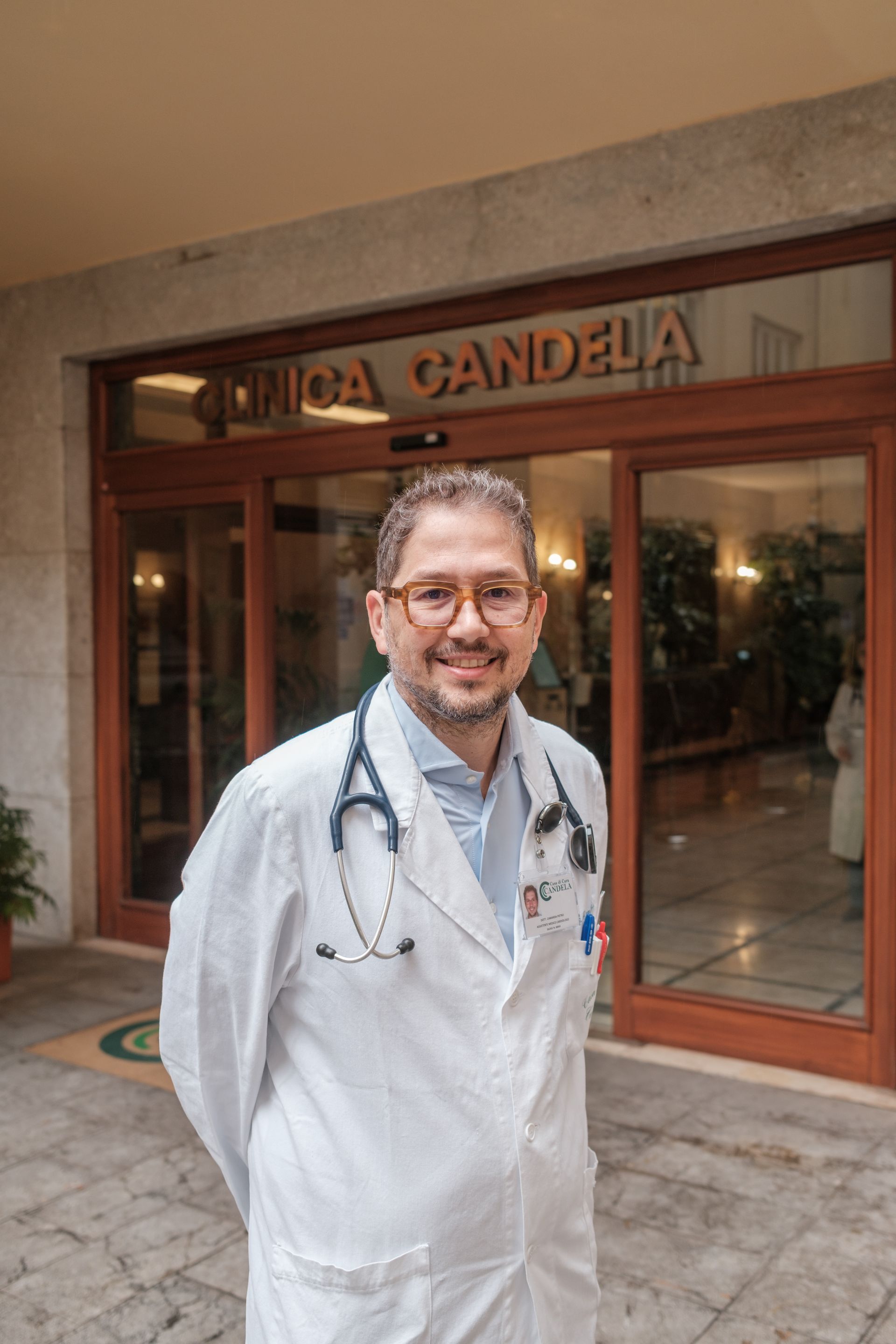 Un uomo in camice e con uno stetoscopio al collo è in piedi davanti a un edificio.