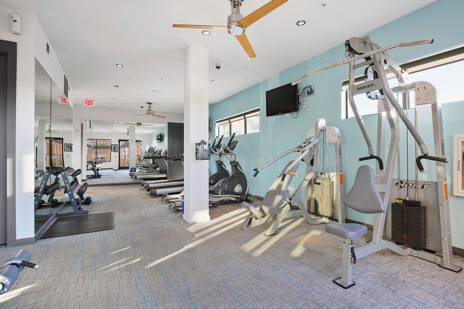 A large gym with a lot of exercise equipment and a ceiling fan.
