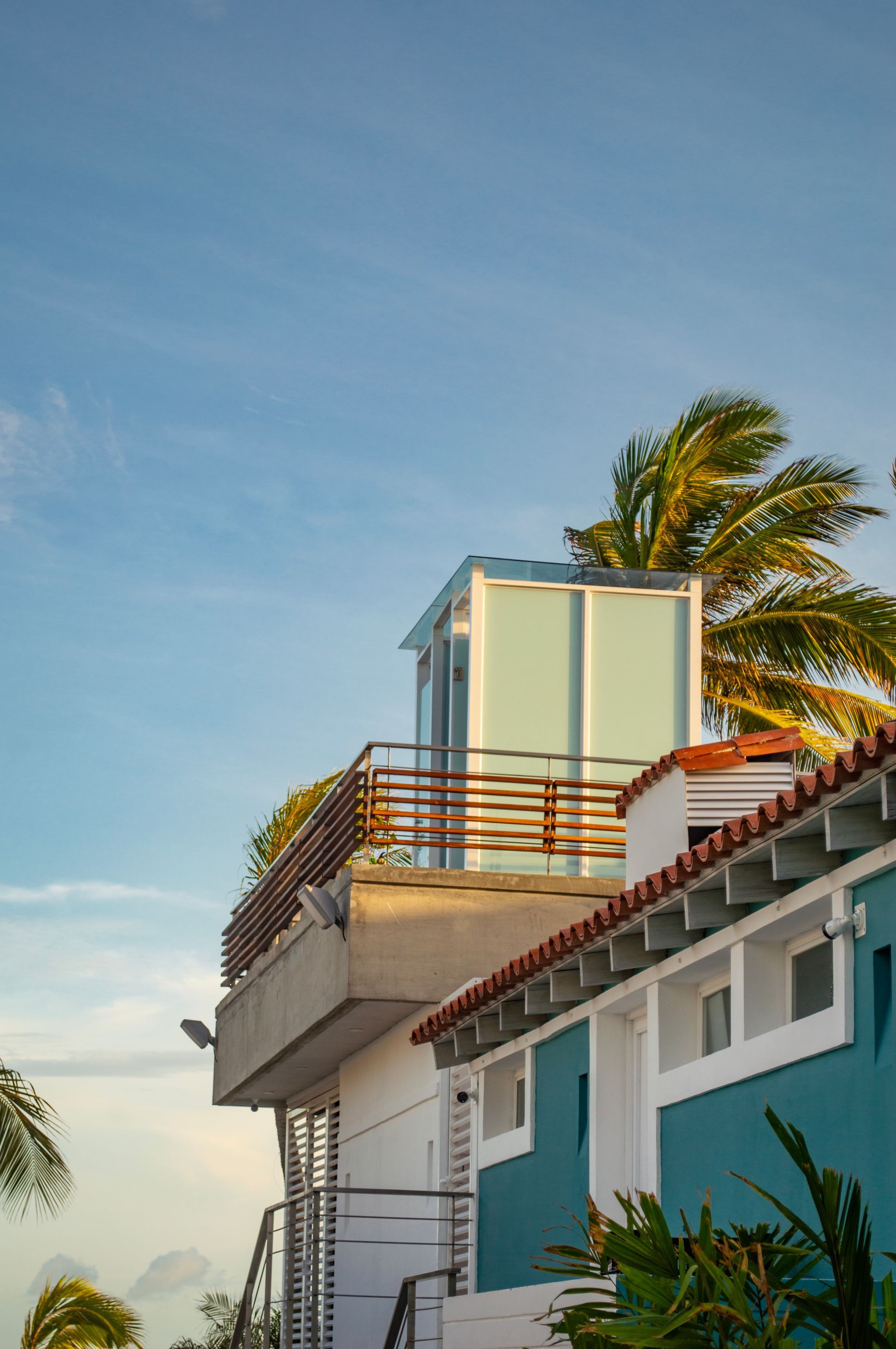 Terraza de hotel en Los Roques con barandilla de cristal y palmera, bajo cielo claro al amanecer.