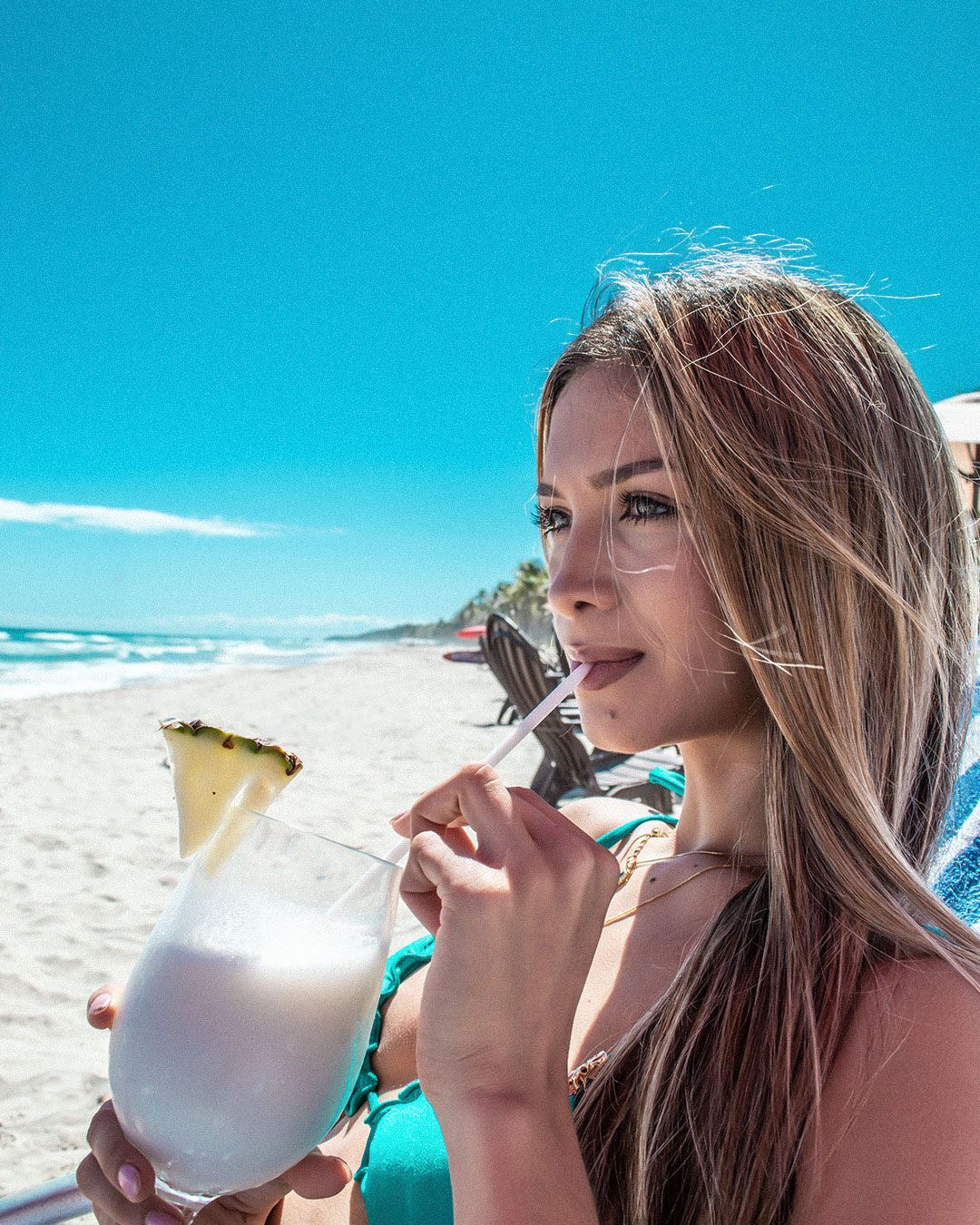 Mujer disfrutando de una fresca piña colada en Playa El Agua, Isla Margarita, bajo el sol caribeño.