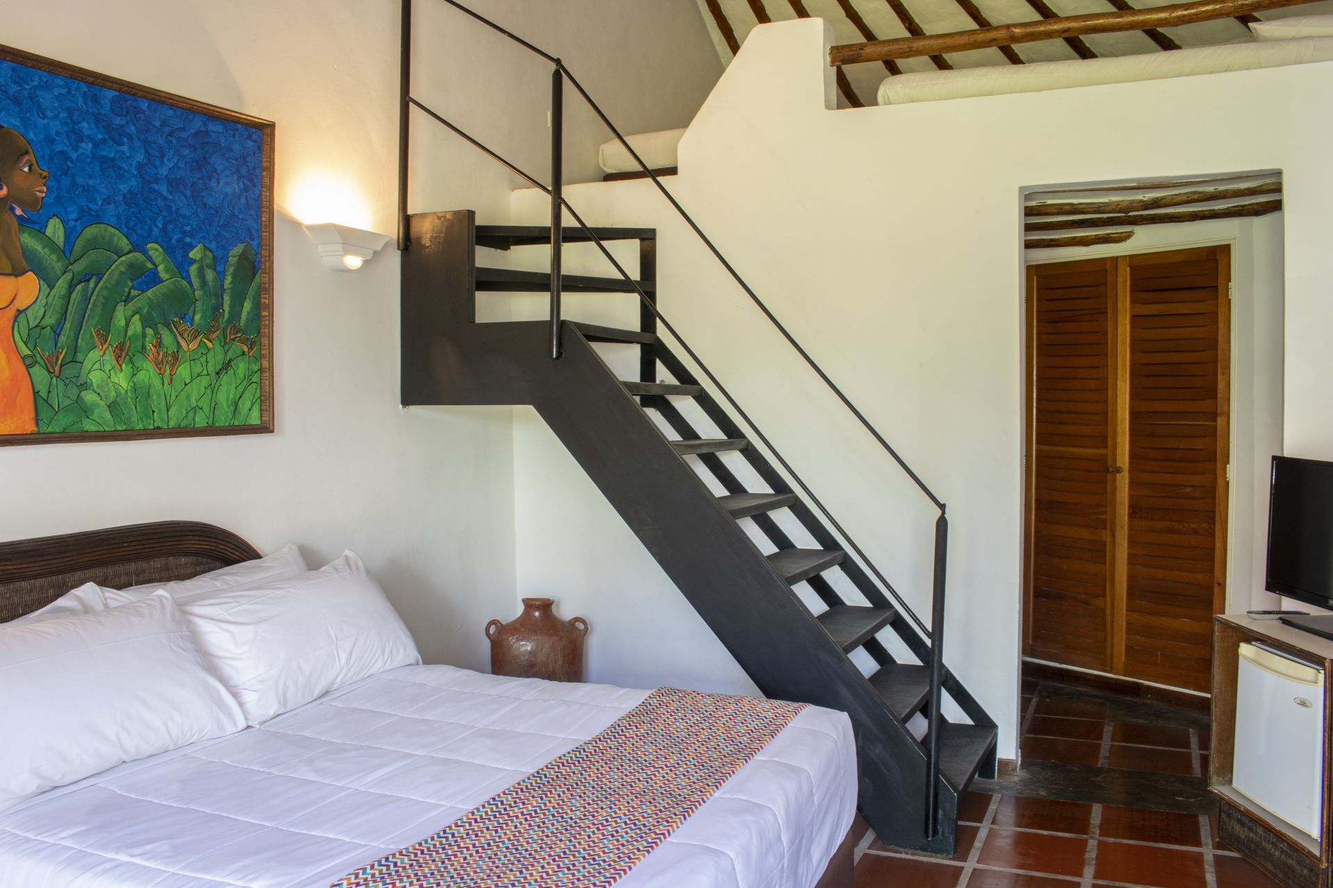 Habitación Bohio en LD Palm Beach, Playa El Agua, con cama blanca, arte azul y escalera metálica a segundo nivel.