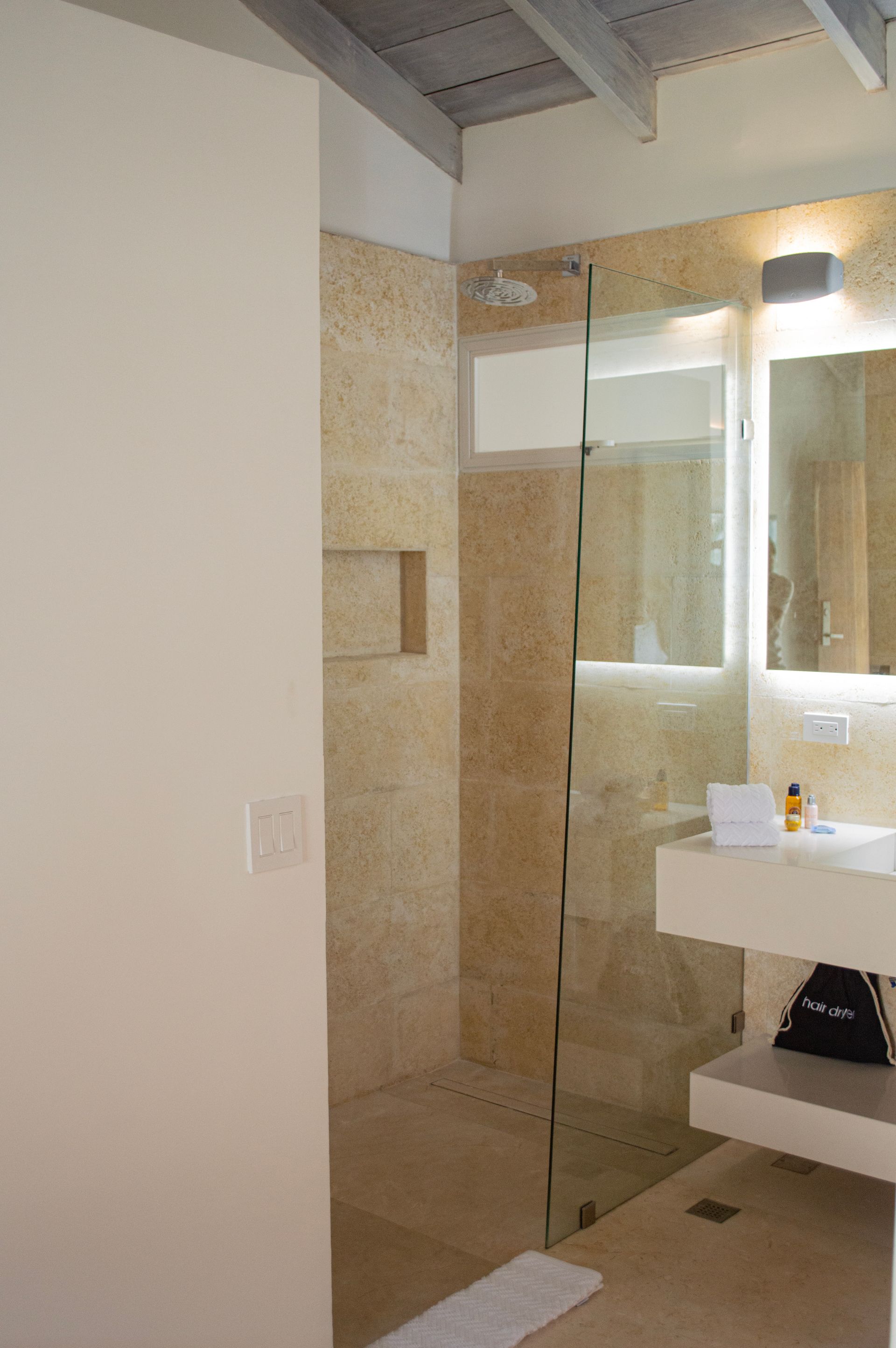 Baño moderno con azulejos beige, ducha de cristal y espejo amplio en hotel de Los Roques.