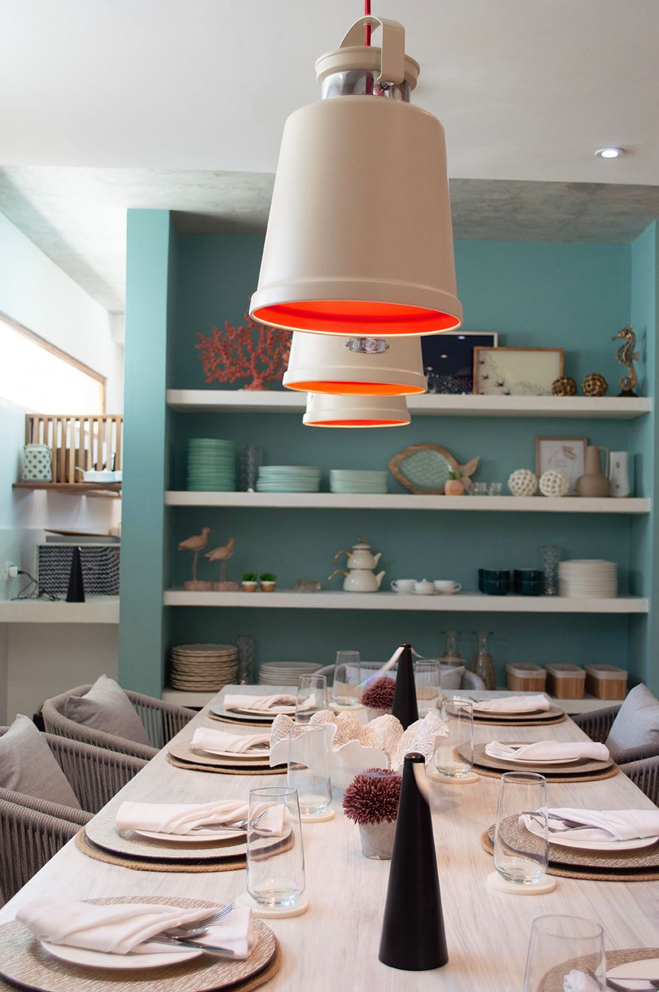 Comedor elegante en Sabbia by LD, Los Roques, con estanterías decorativas y lámpara colgante naranja.