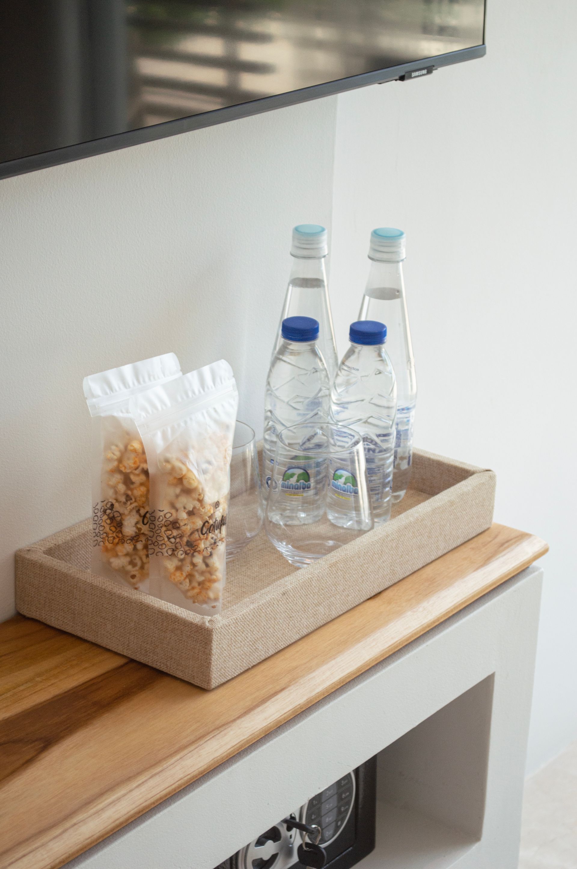 Snack de bienvenida en hotel de Los Roques, con botellas de agua y granola, presentados en bandeja tejida para los huéspedes.