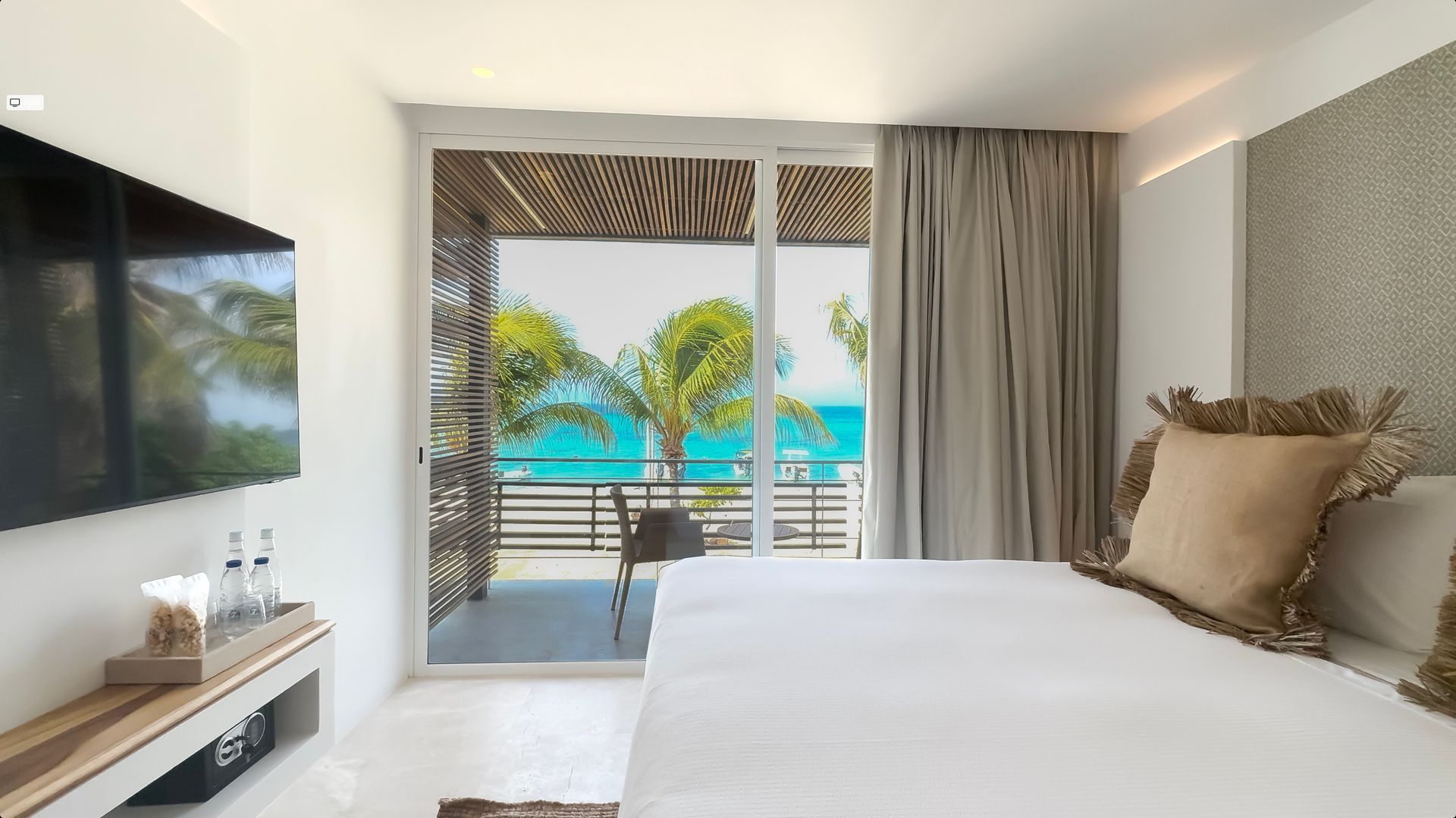 Habitación superior en Macanao Lodge con cama amplia, TV plana y balcón con vista al mar Caribe y vegetación tropical.