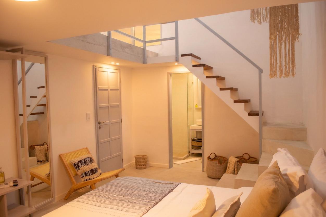 Habitación con cama grande, ropa de cama blanca y estampada, y ventana con persianas cerradas.