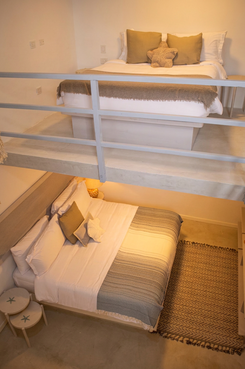 Habitación con cama grande, ropa de cama blanca y estampada, y ventana con persianas cerradas.