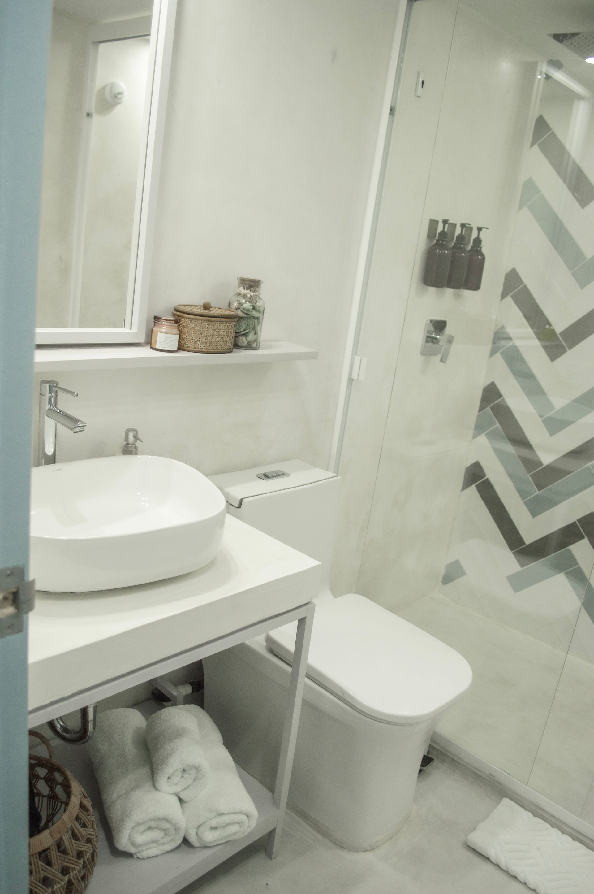 Baño moderno con lavabo de vasija, grifo de pared y ducha con puertas de vidrio.