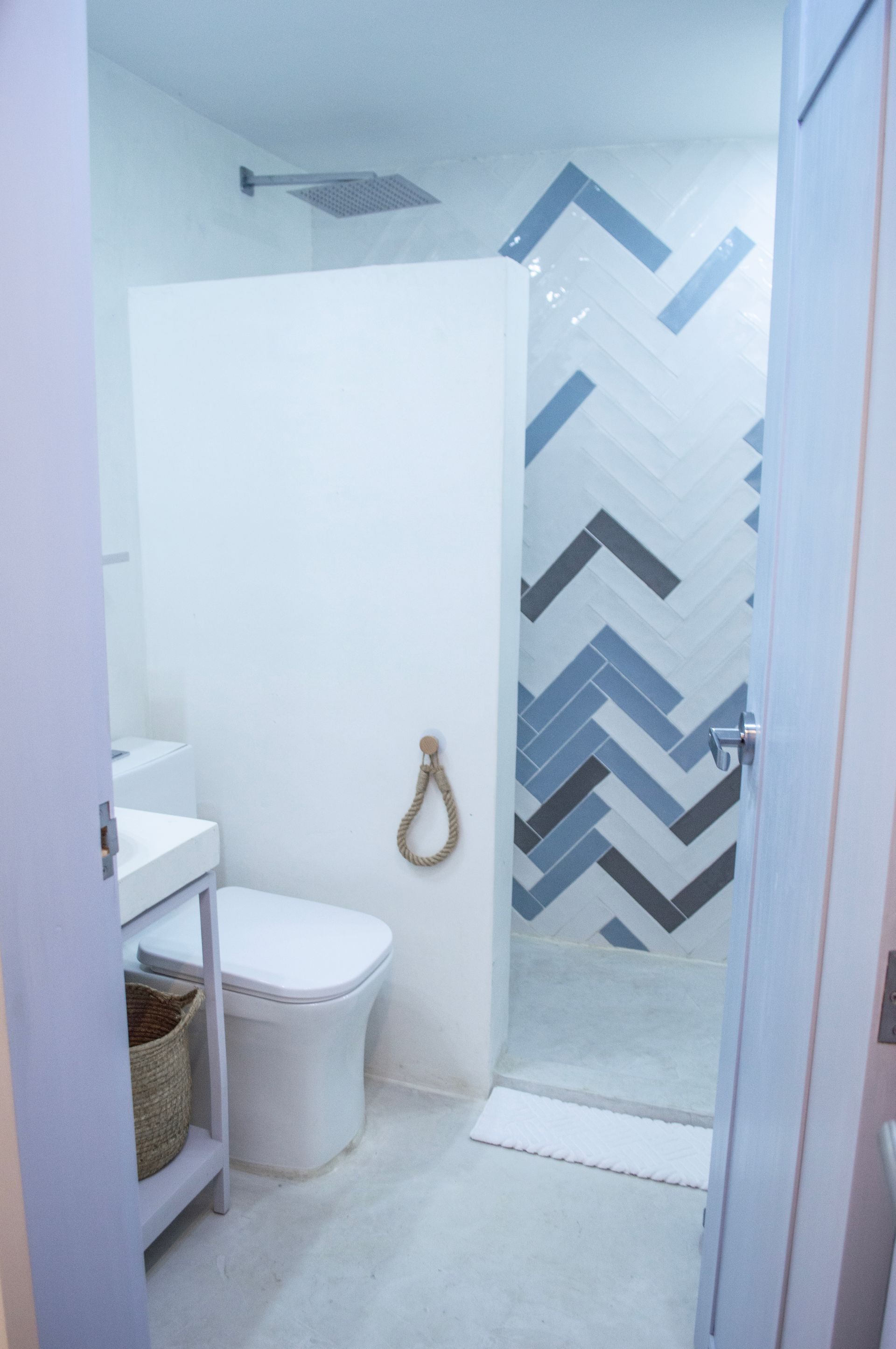Baño moderno con lavabo, inodoro y ducha con patrones geométricos en azul y gris.