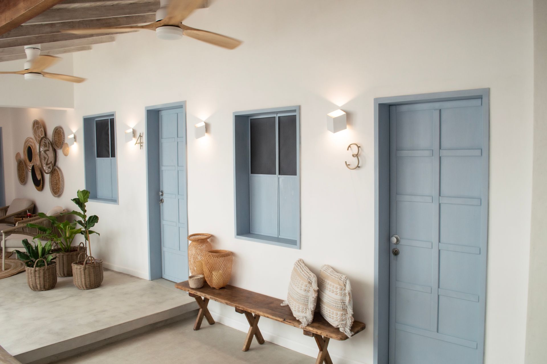 Pasillo del hotel con puertas azules numeradas, banco de madera y decoración minimalista.