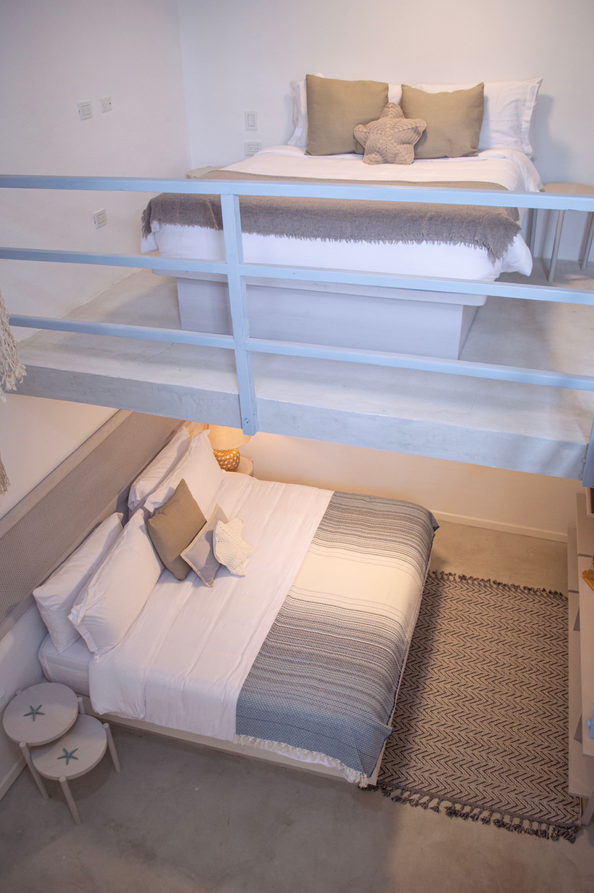 Habitación con cama grande, ropa de cama blanca y estampada, y ventana con persianas cerradas.