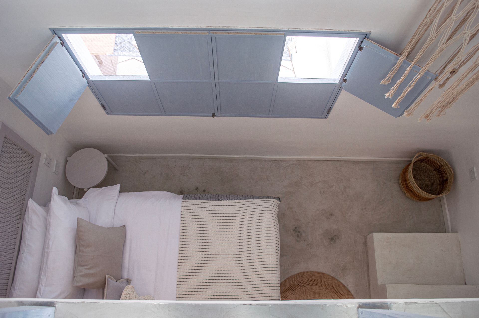 Habitación con cama grande, ropa de cama blanca y estampada, y ventana con persianas cerradas.