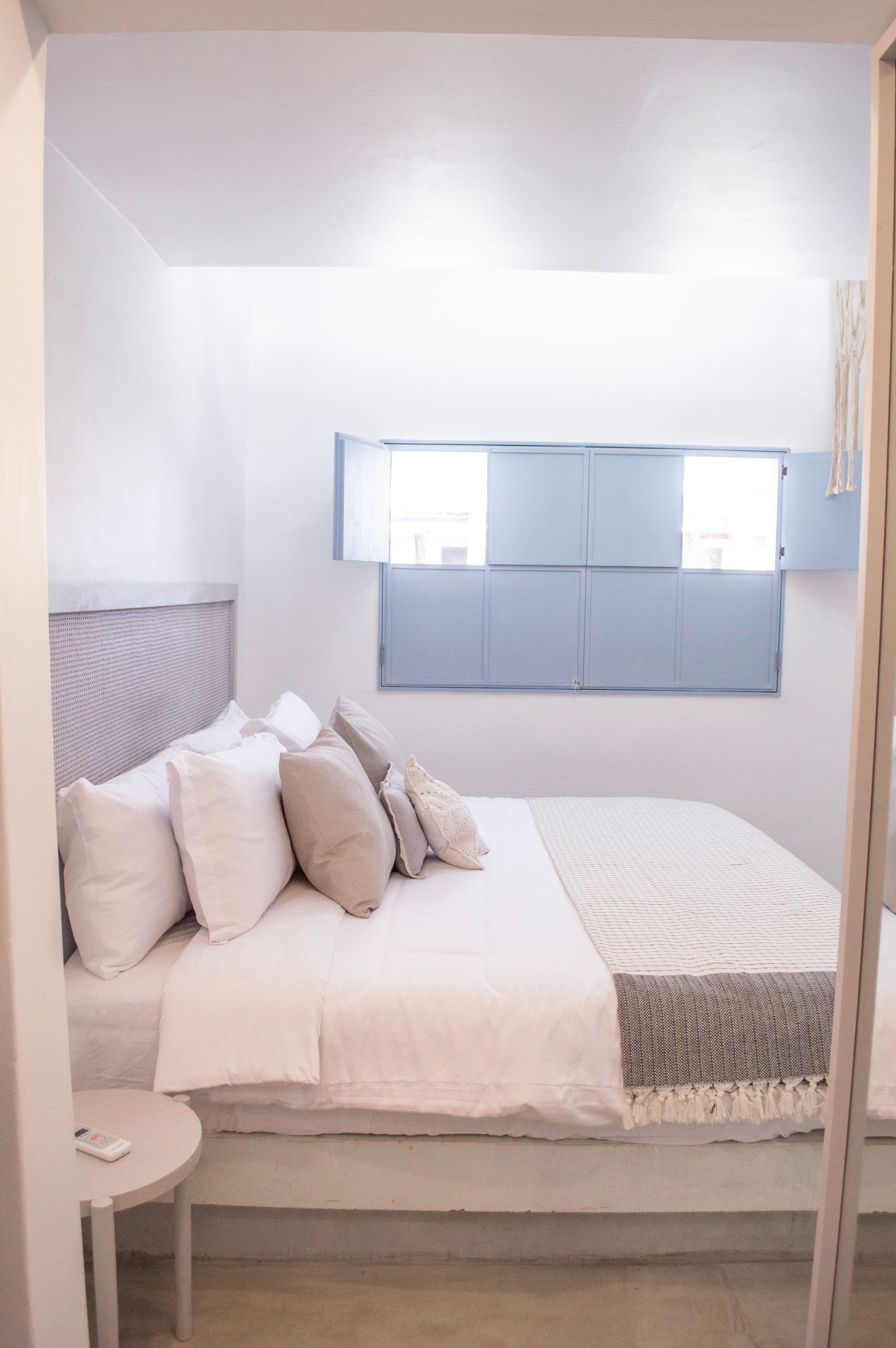 Habitación con cama grande, ropa de cama blanca y estampada, y ventana con persianas cerradas.