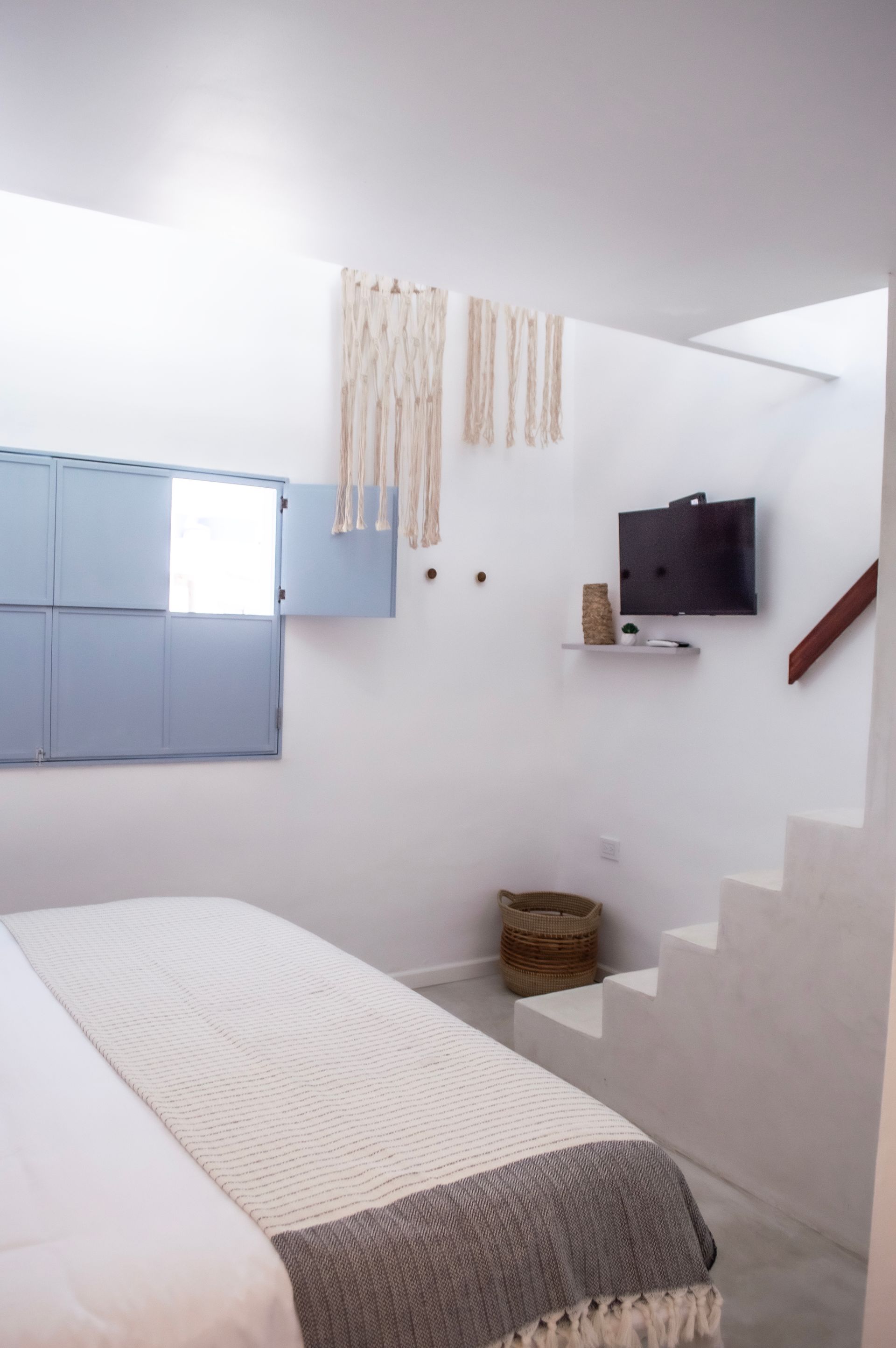 Habitación con cama grande, ropa de cama blanca y estampada, y ventana con persianas cerradas.
