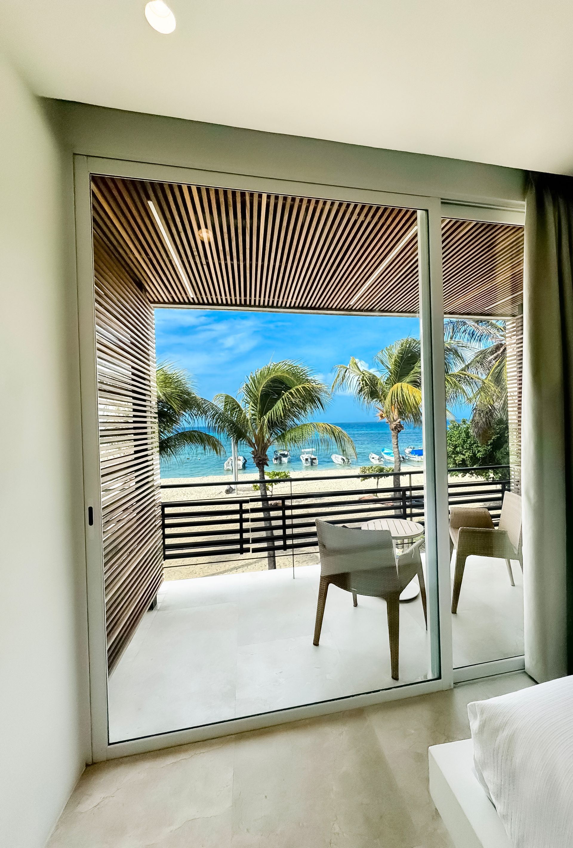 Vista panorámica desde habitación del Hotel Macanao Lodge, con cortinas blancas, balcón acogedor y playa caribeña.