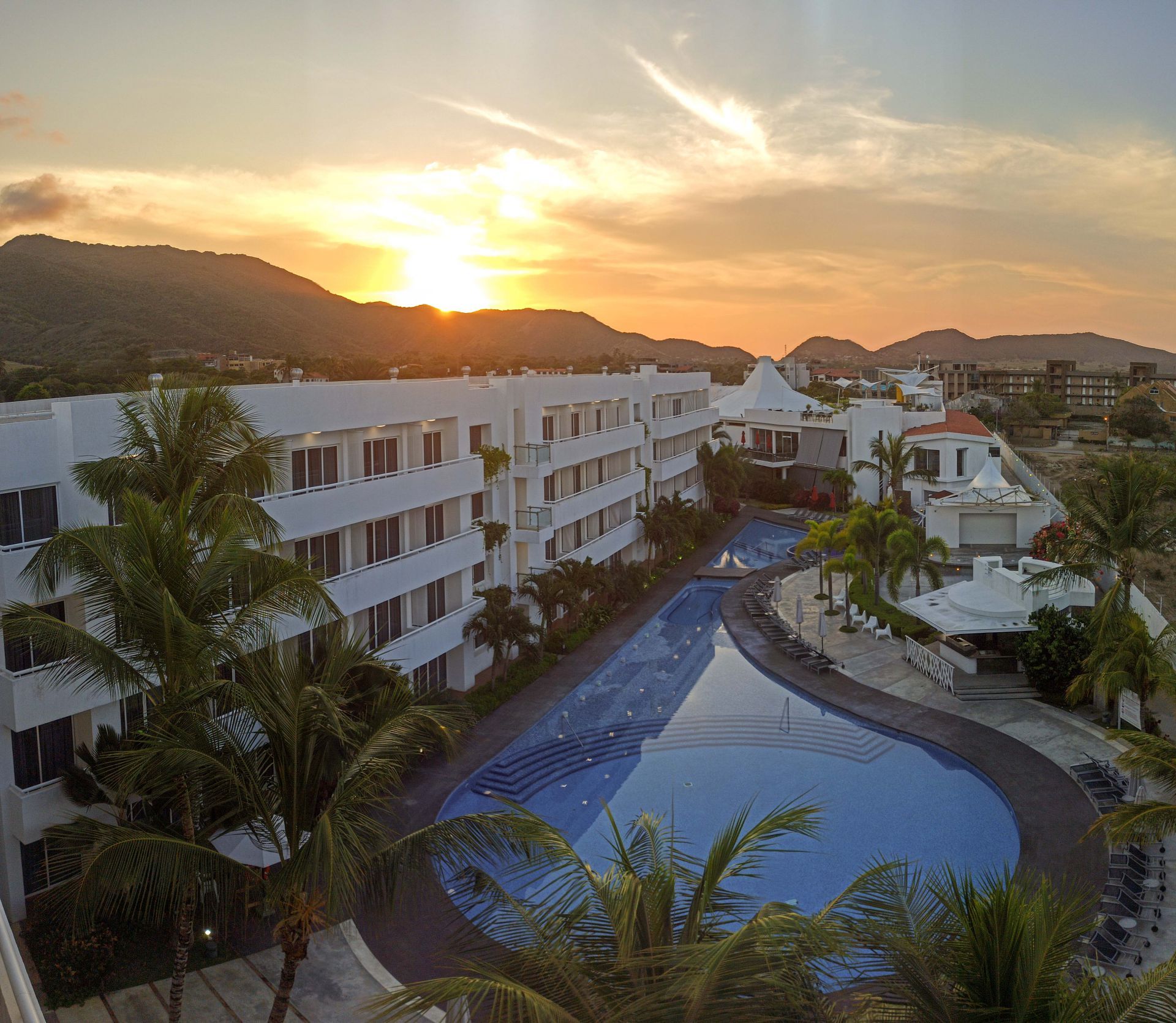 Vista aérea del hotel LD PLUS en Playa el Agua al atardecer, con piscina serpenteante y exuberante vegetación tropical.