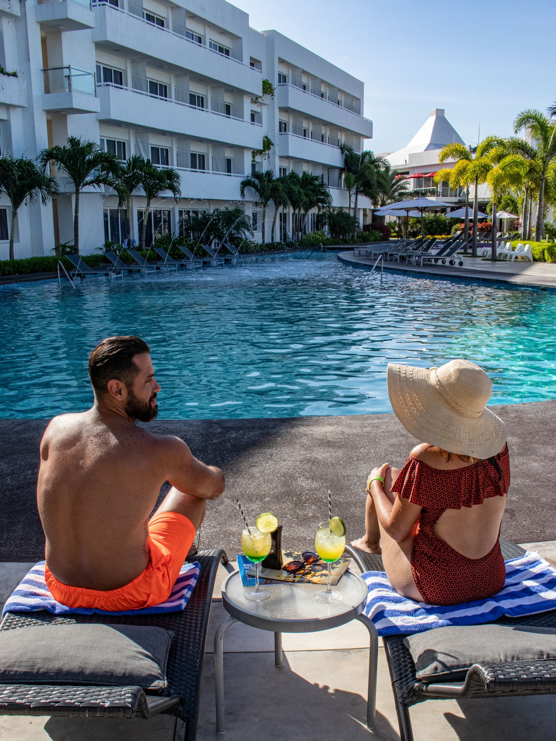 Pareja disfrutando de la piscina en LD PLUS, Playa El Agua, Isla Margarita. Ambiente relajante y bebidas refrescantes.