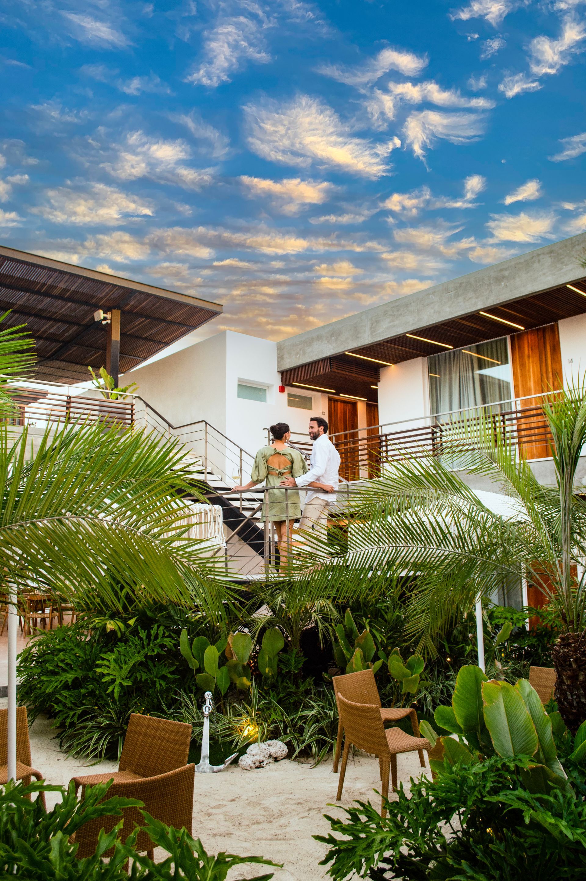 Pareja de pie en escalera exterior del hotel Macanao Lodge By LD, rodeados de vegetación tropical.