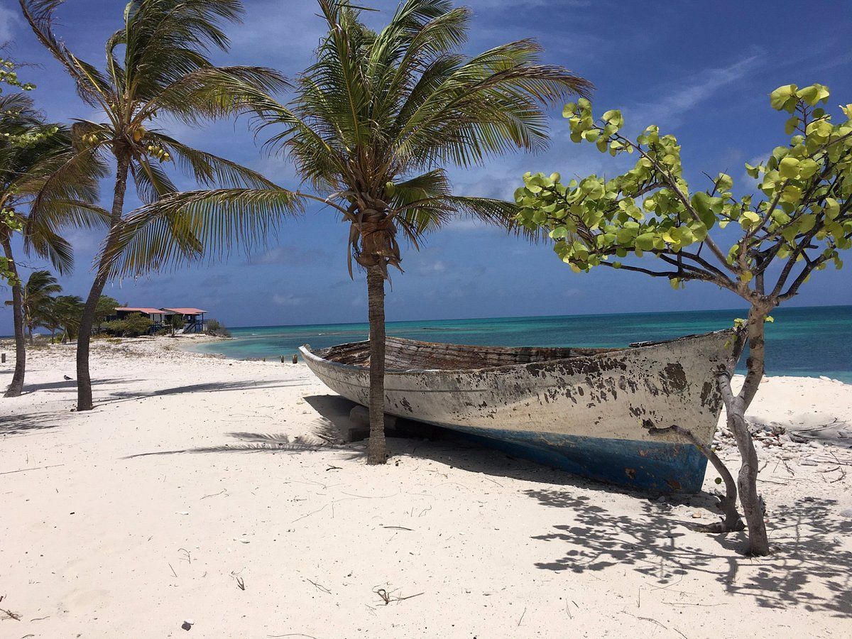 Playa en Los Roques con bote abandonado en la arena blanca y aguas turquesas de fondo.