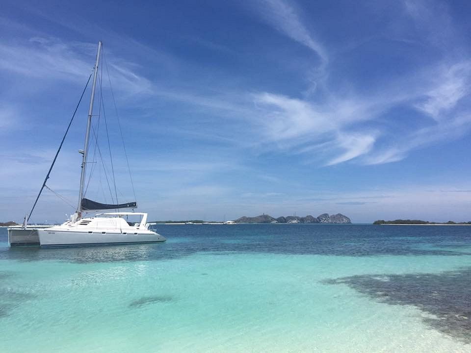 Catamarán blanco navegando en aguas turquesas de Los Roques, con islas en el horizonte y cielo despejado.