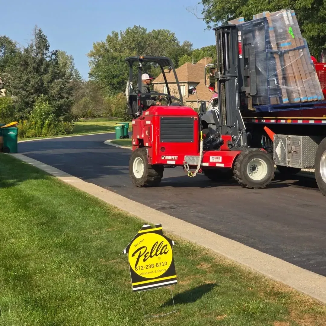 Red service truck loading large wrapped pallets on a suburban street beside a lawn sign.