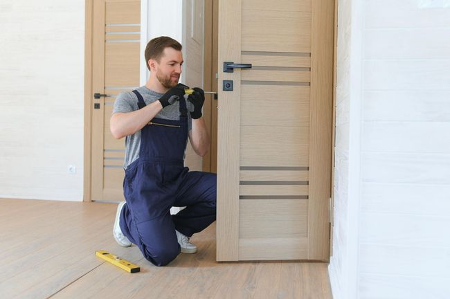 Worker installing a door frame with tools in a bright room