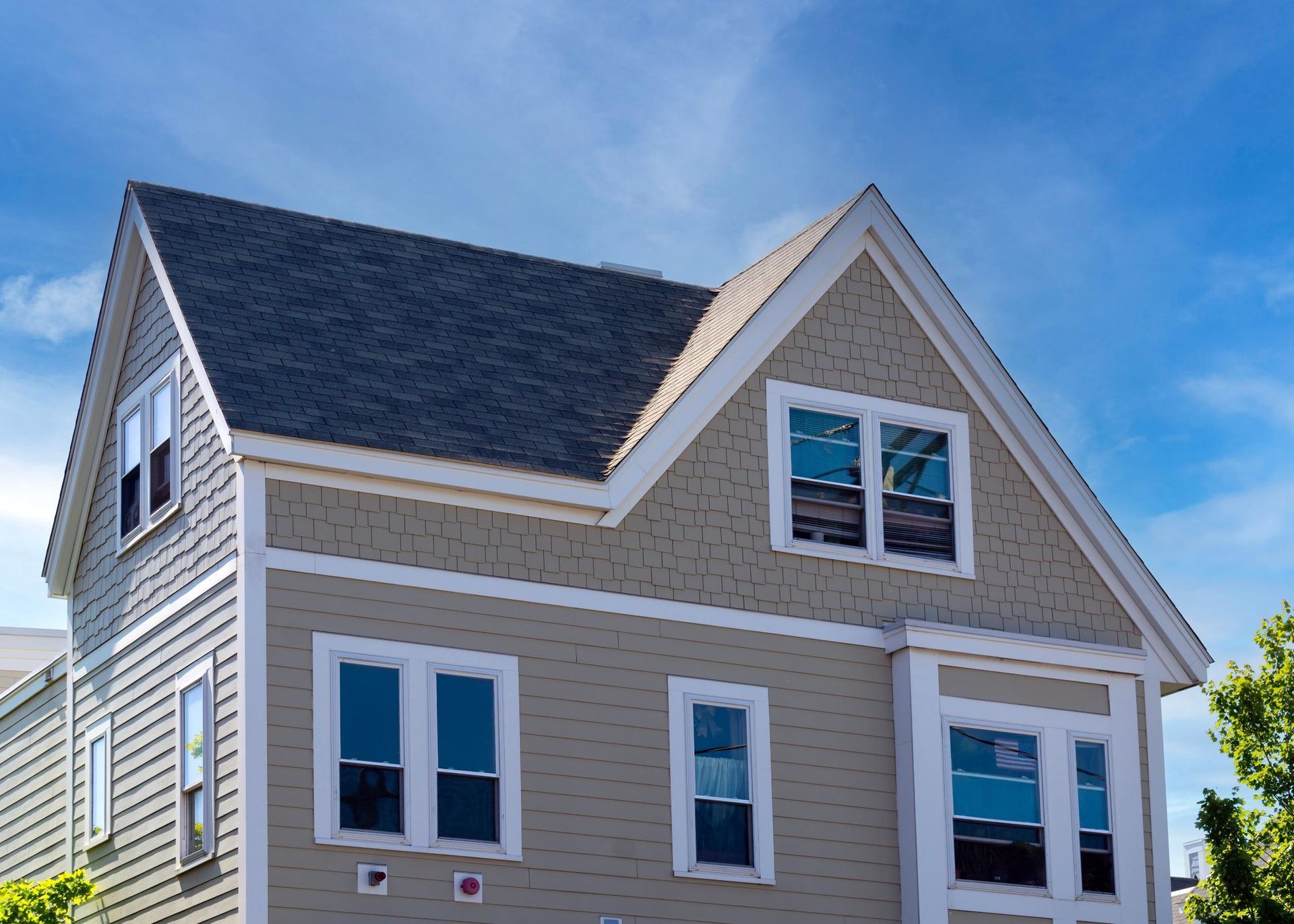 Gray house with dark roof and white-trimmed windows against a blue sky