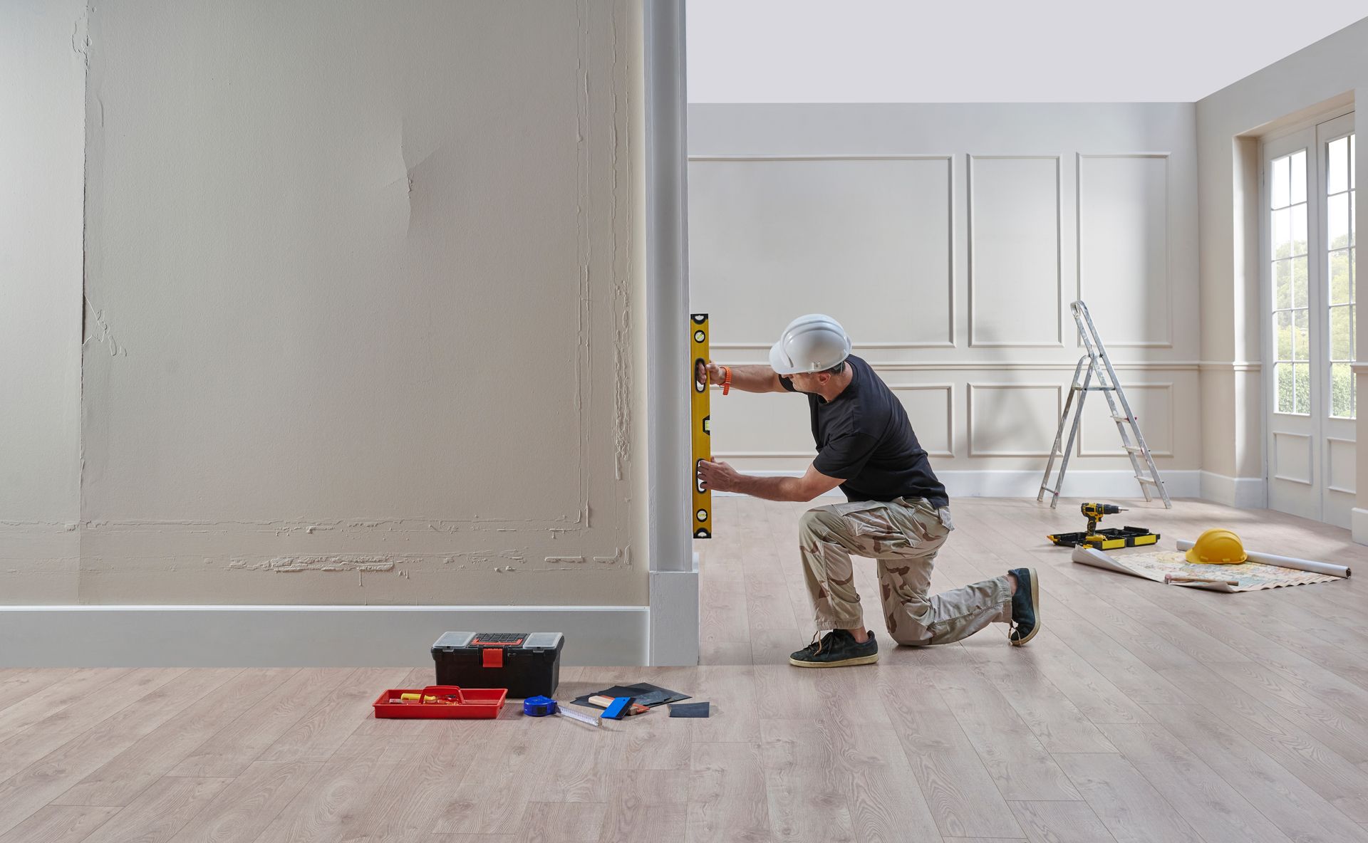 A Man is Measuring a Wall With a Level in an Empty Room