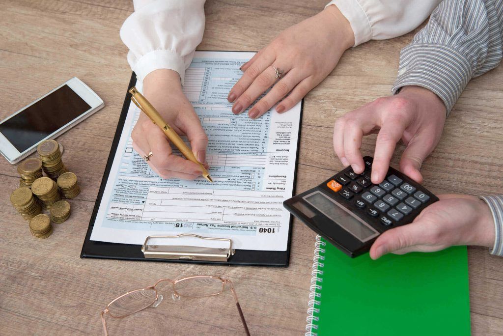 Man in suit loading luggage into a white limousine's trunk at an airport.