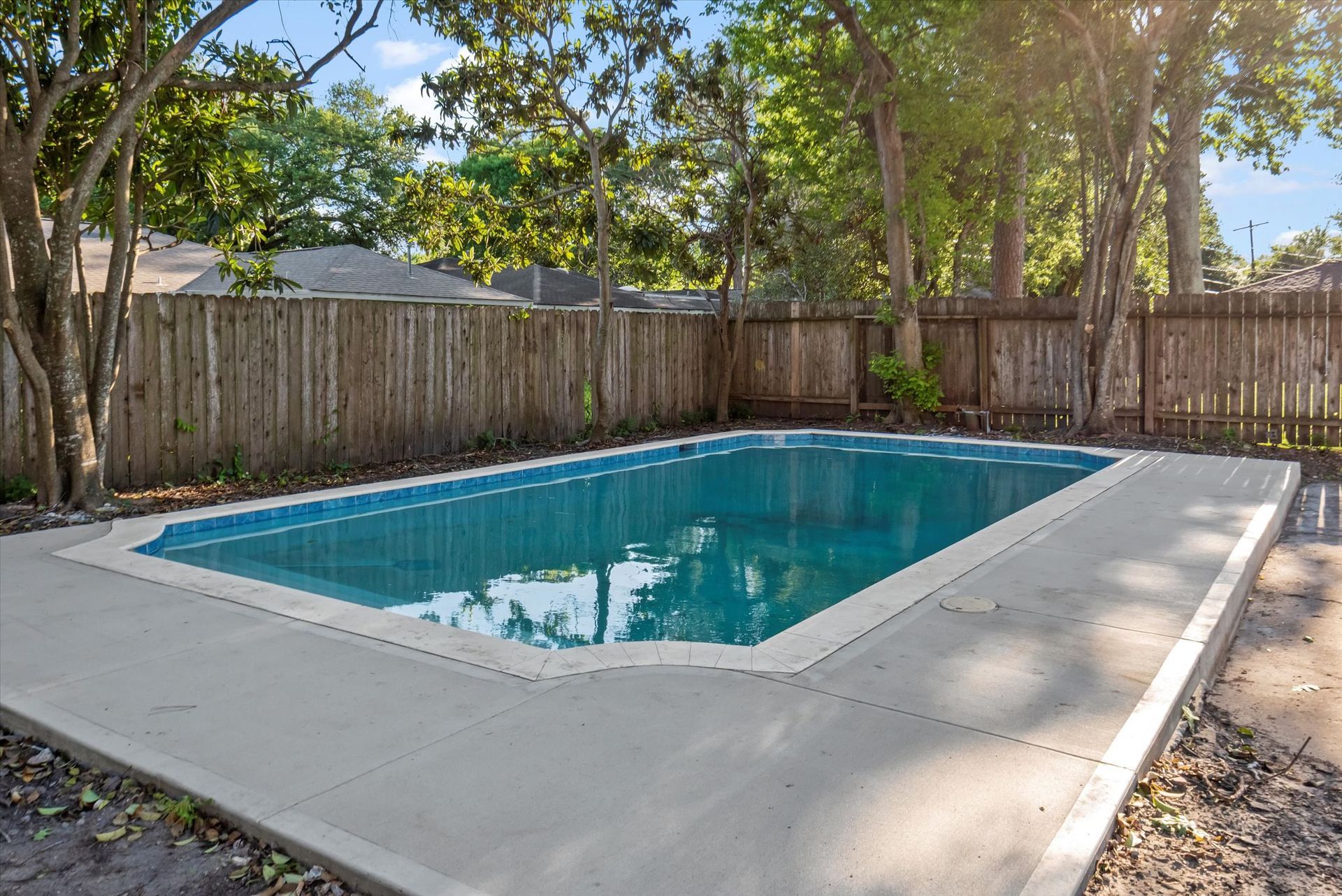 A large swimming pool is surrounded by trees and a wooden fence.