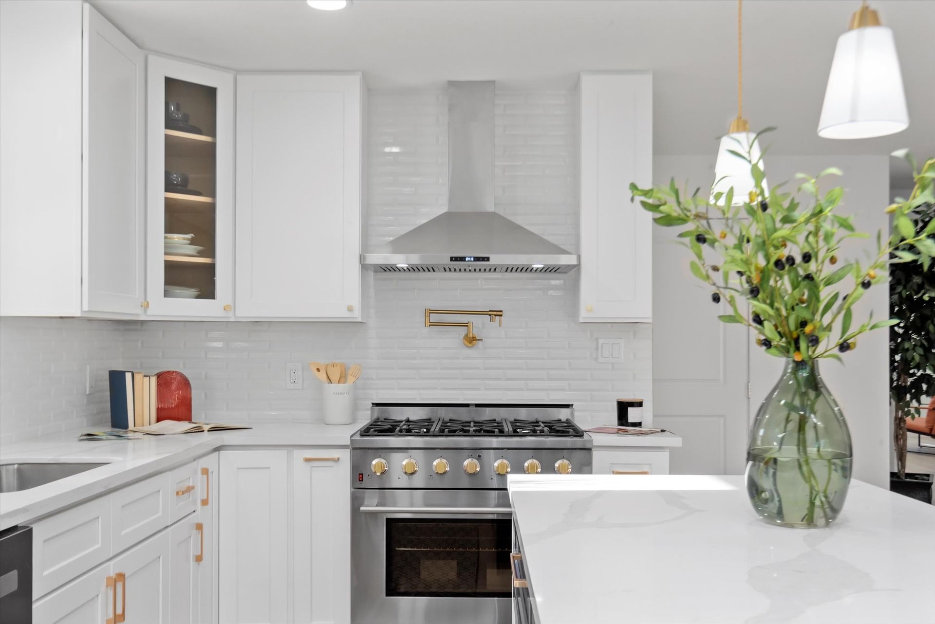 A kitchen with white cabinets , stainless steel appliances , and a vase of flowers on the counter.