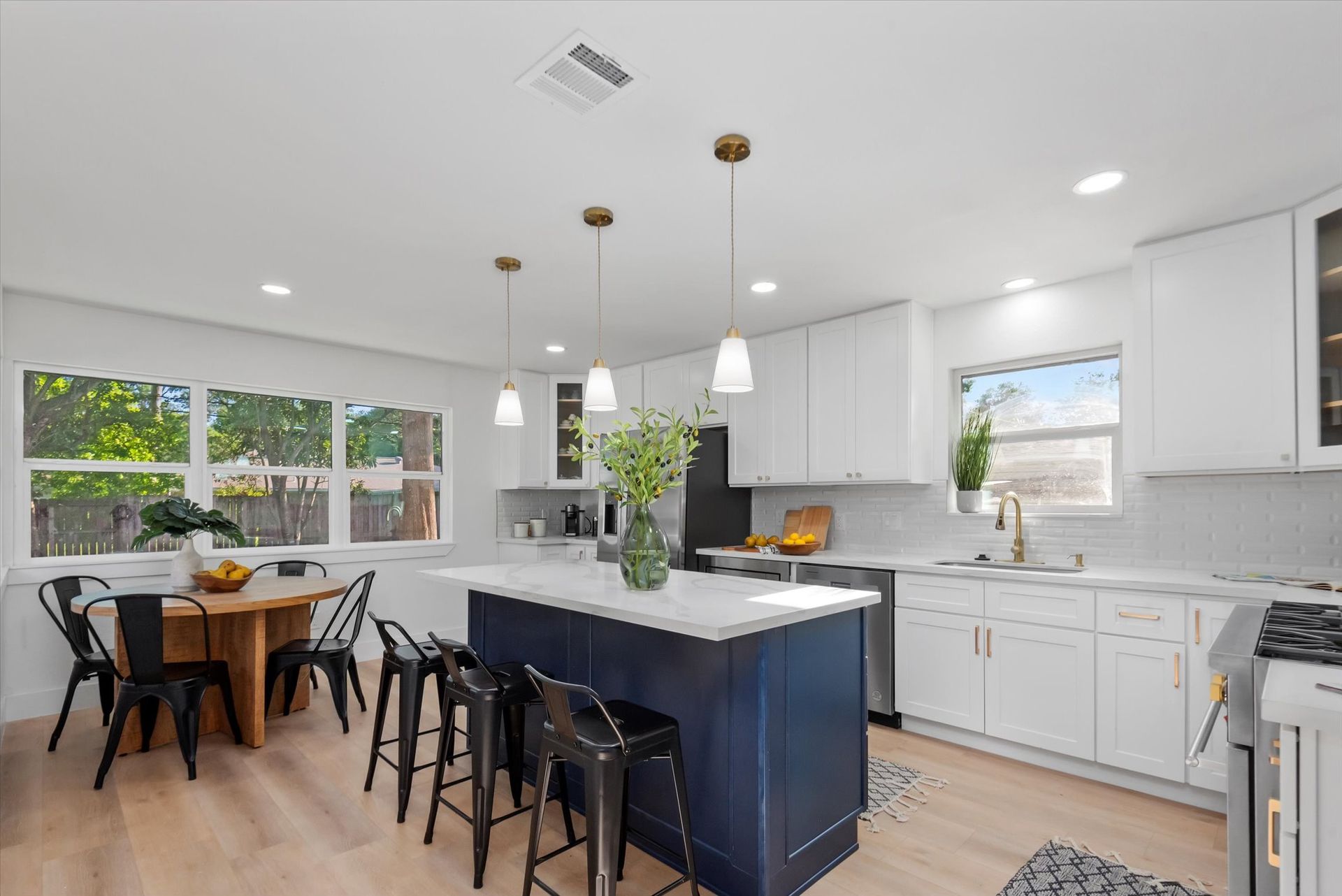 A kitchen with white cabinets , a blue island , a table and chairs.