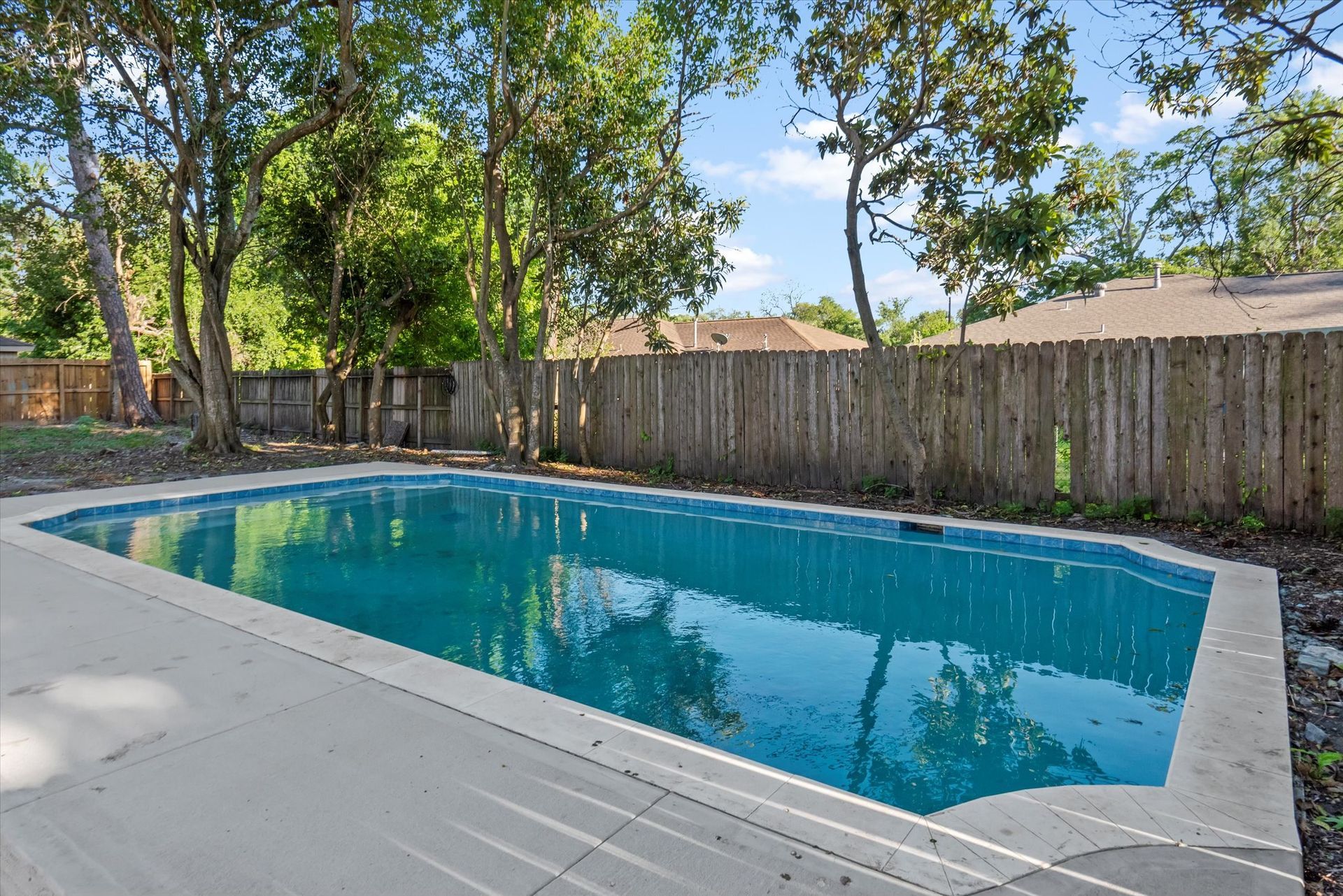 A large swimming pool is surrounded by trees and a wooden fence.