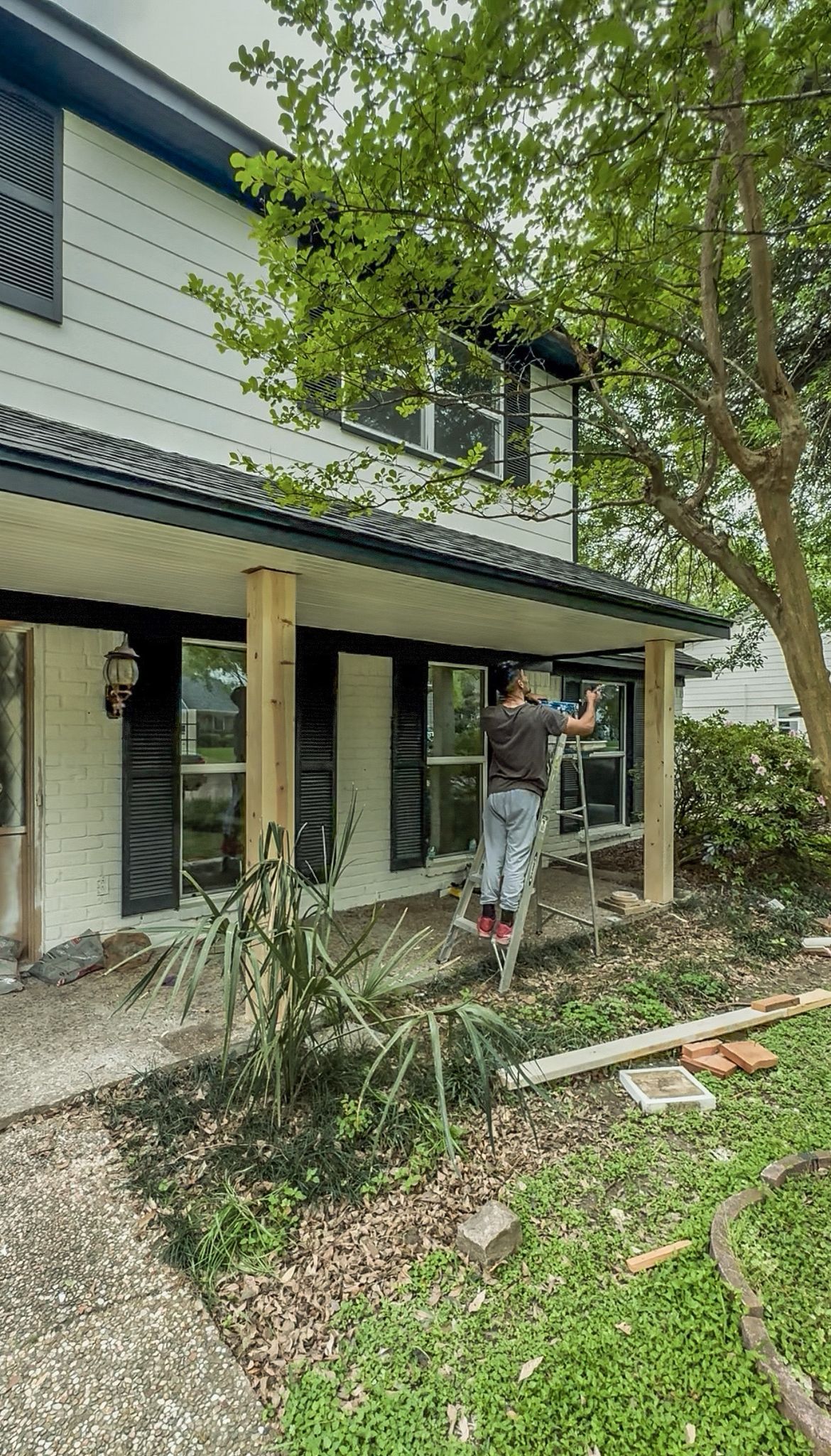 A man is standing on a porch of a house painting a window.