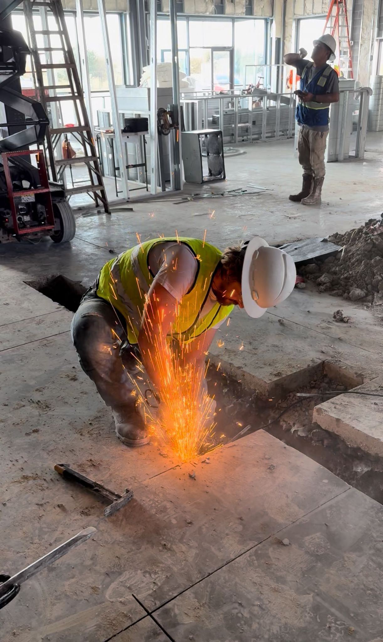 A construction worker is welding a piece of metal in a hole in the floor.