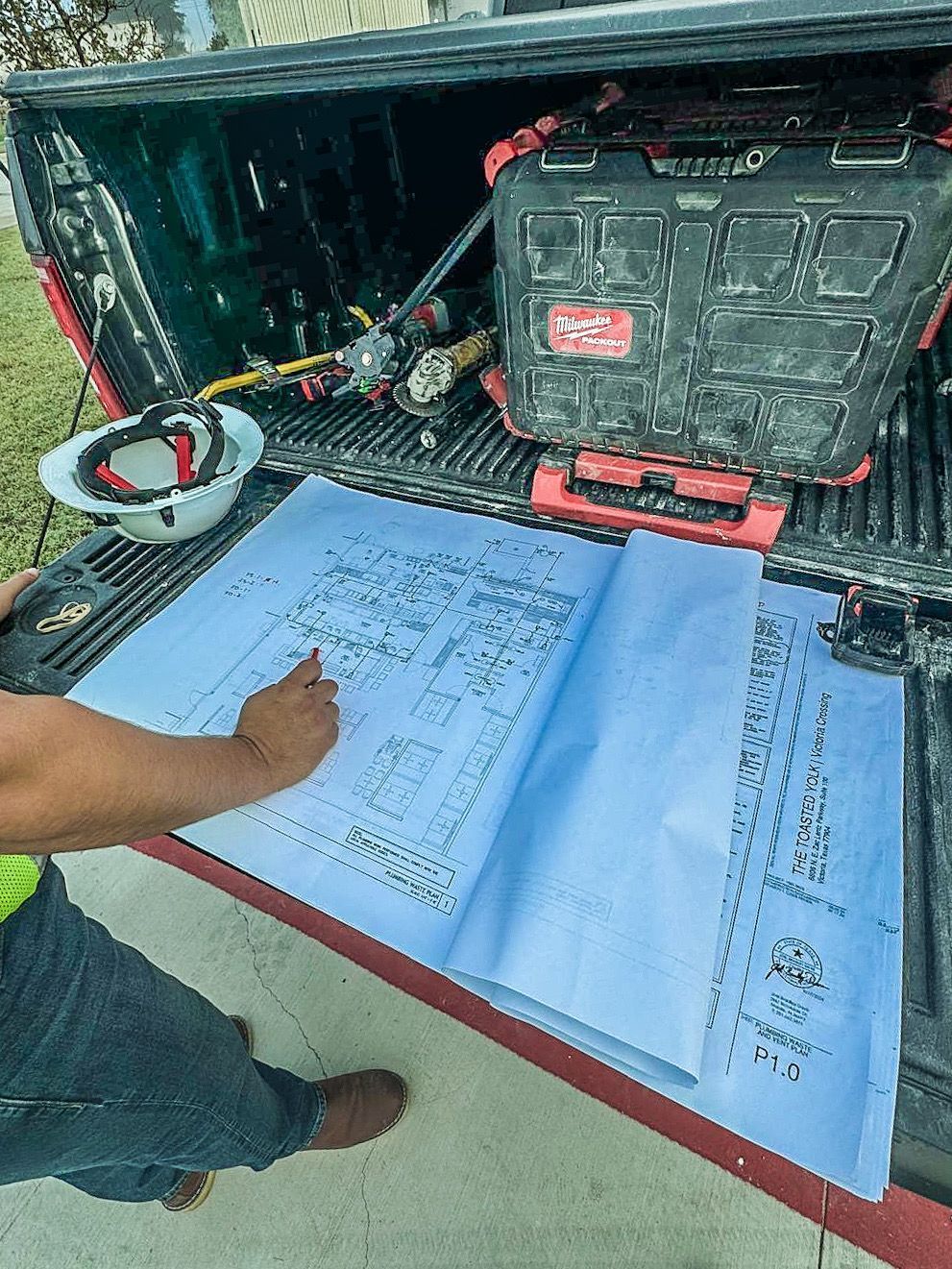 A Bilingual Contractor is writing on a blueprint in the back of a truck.