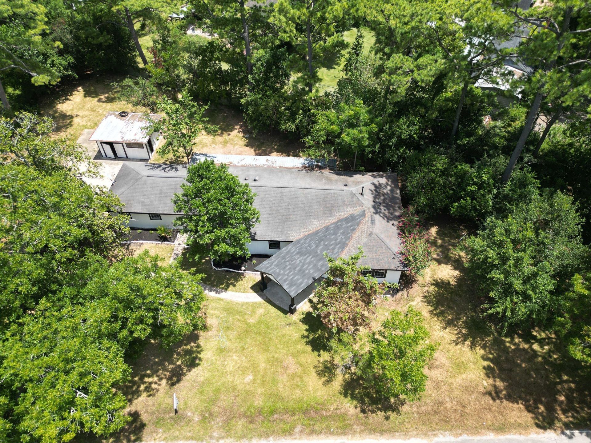 Aerial view of a house with a gray roof, surrounded by green trees and grass.